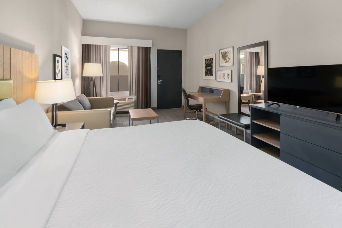 Ein Hotelzimmer mit einem großen Bett, einem Schreibtisch, einem Sessel, einem Fernseher und einem Kleiderschrank.