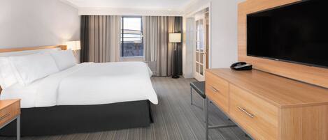 A hotel room with a large bed, a flat-screen TV, a wooden dresser, and a window with curtains.