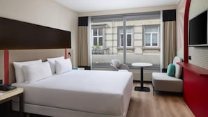 A hotel room with a large bed, a desk with a telephone, a chair, a small table, and a TV mounted on the wall. - iStay by NH Brussels Stéphanie (Brussels)