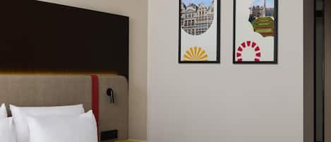 A hotel room with a bed, a bedside table, and two framed pictures on the wall.