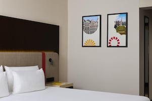 Una camera d'albergo con un letto, un comodino e due quadri appesi al muro.