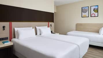 Habitación de hotel con dos camas, una mesita de noche, una lámpara y dos cuadros en la pared.