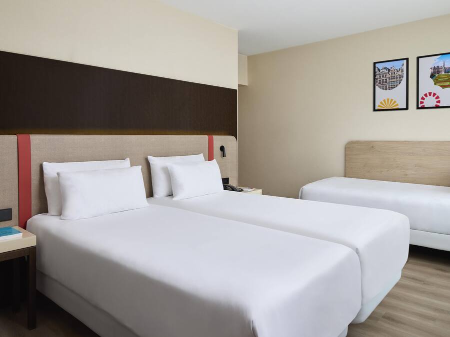 Een hotelkamer met twee bedden, een nachtkastje, een lamp en twee ingekaderde foto’s aan de muur.