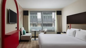 A hotel room with a large bed, a small table, a TV mounted on the wall, and a balcony with curtains. - iStay by NH Brussels Stéphanie (Brussels)