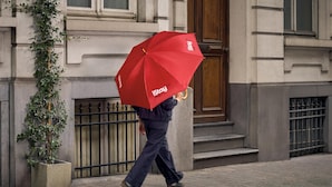 A person walking on a sidewalk with a red umbrella, a building with a wooden door, and a metal gate. - iStay by NH Brussels Stéphanie (Brussels)