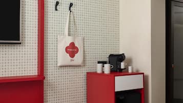 Een hotelkamer met een kleurenschema van rood en wit, een koffieapparaat en een witte boodschappentas hangend aan de muur.