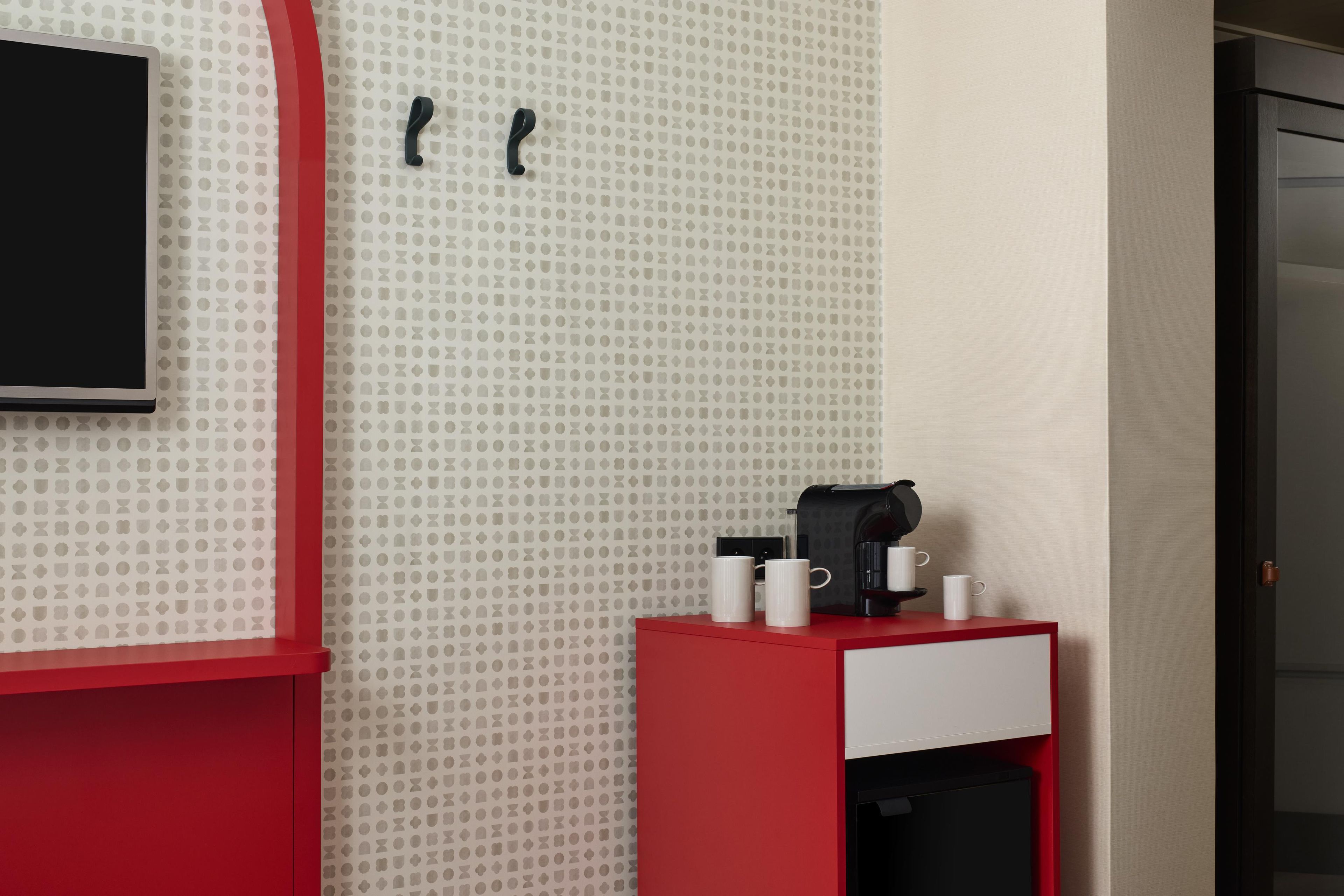 Habitación de hotel con decoración roja y blanca, una cafetera y dos tazas sobre una mesita.