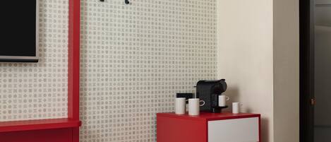 Habitación de hotel con decoración roja y blanca, una cafetera y dos tazas sobre una mesita.