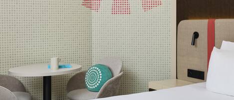 A hotel room with a bed, a small table, a chair, and a wall with a geometric pattern.