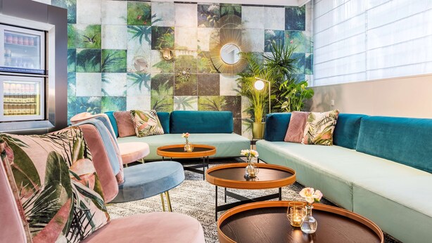 Una sala moderna con sofás color turquesa, mesas redondas para café y una pared con temática tropical.