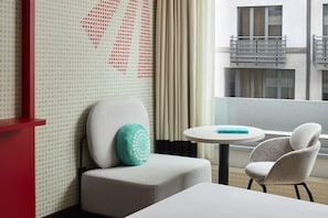A hotel room with a sofa, a small table, and a view of the building's exterior. - iStay by NH Brussels Stéphanie (Brussels)