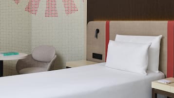 Une chambre d’hôtel avec un lit, une chaise, une petite table et un mur orné d’un motif géométrique.