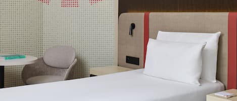 A hotel room with a bed, a chair, a small table, and a wall with a geometric pattern.