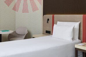 A hotel room with a bed, a chair, a small table, and a wall with a geometric pattern. - iStay by NH Brussels Stéphanie (Brussels)
