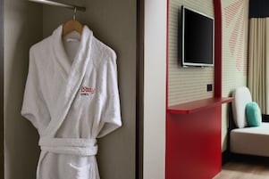 Un accappatoio bianco appeso a un gancio in una stanza con una scrivania rossa per la reception e un televisore fissato al muro.