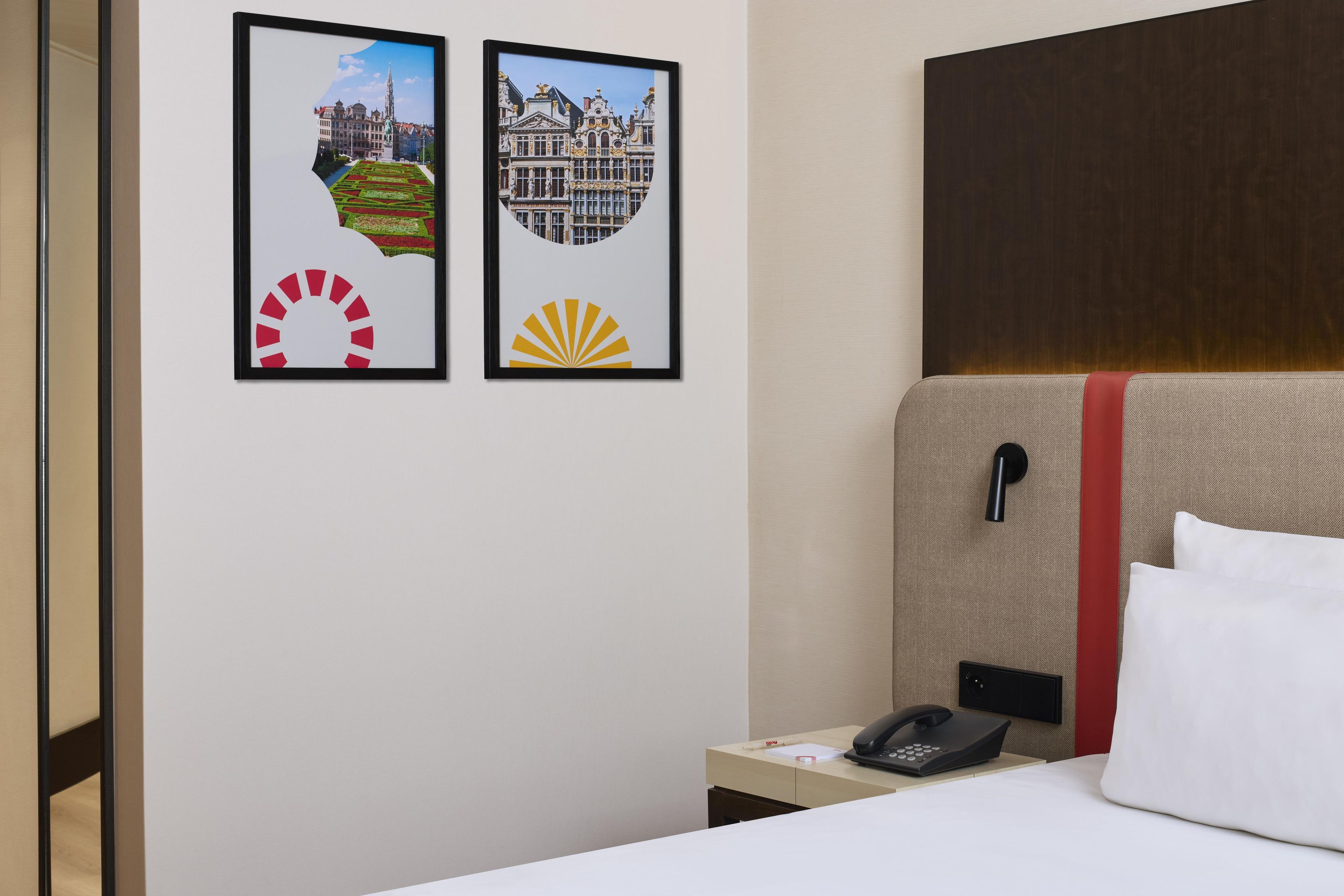 Een hotelkamer met een bed, een bureau met een telefoon en twee ingelijste foto's aan de muur.