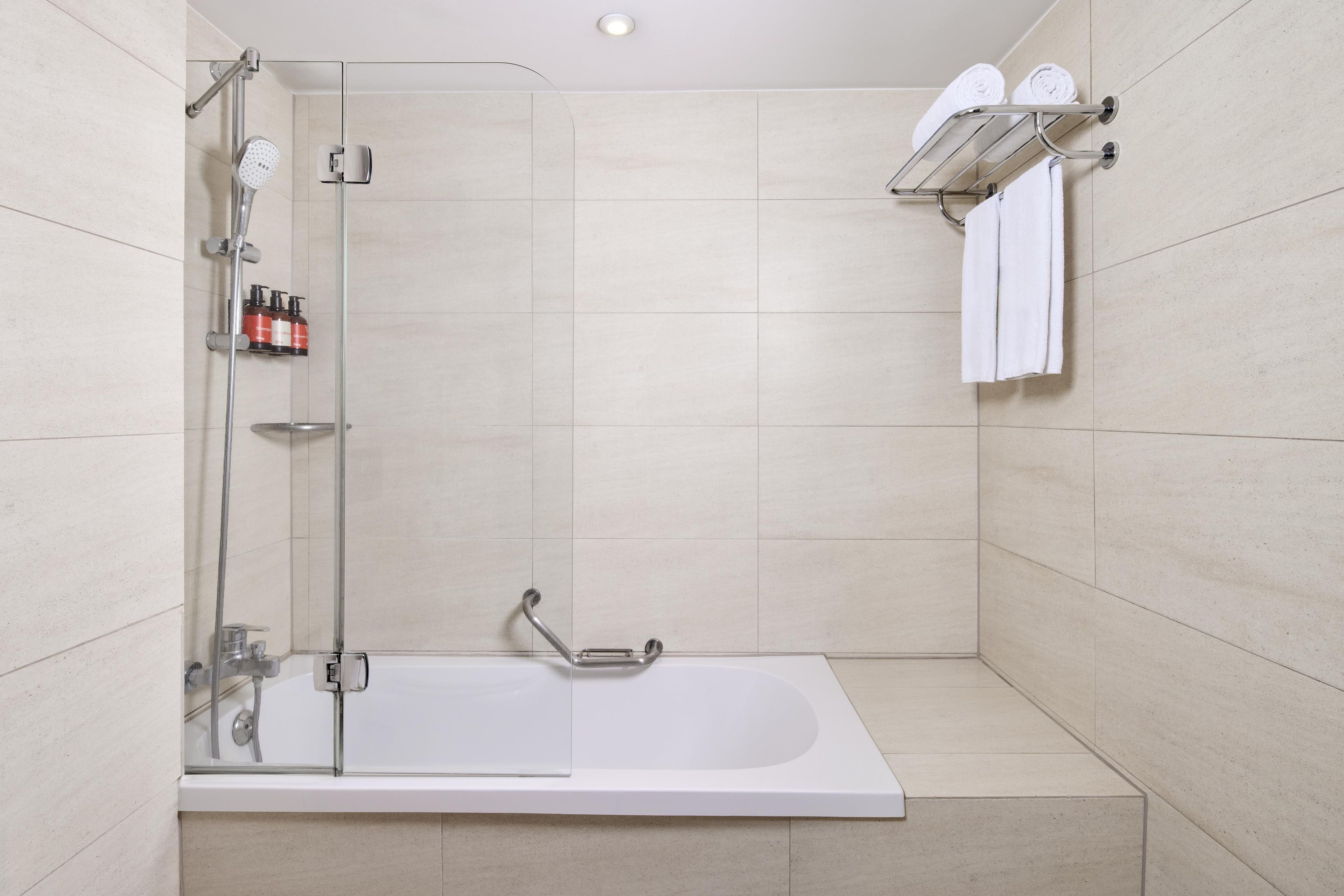 Een moderne badkamer met een douchekabinet van glas, een witte badkuip en een handdoekhouder.