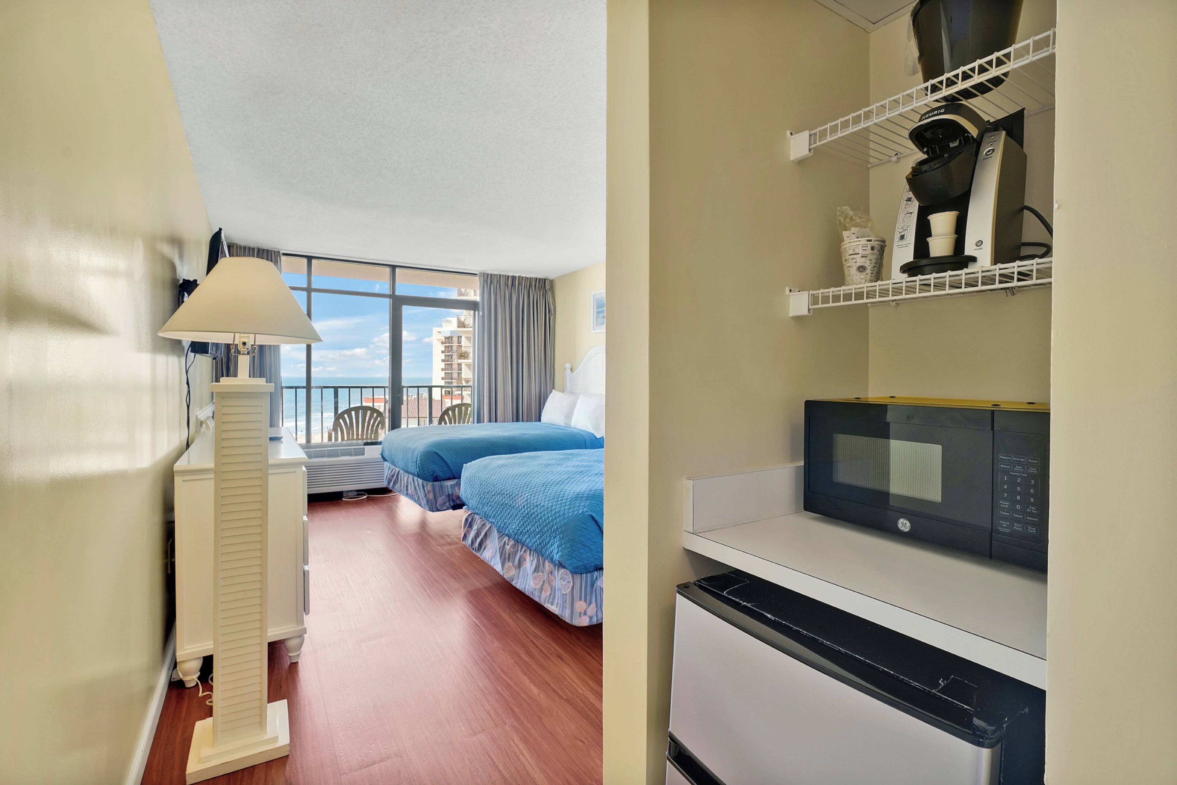 A hotel room with two beds, a microwave, a coffee maker, and a view of the city.