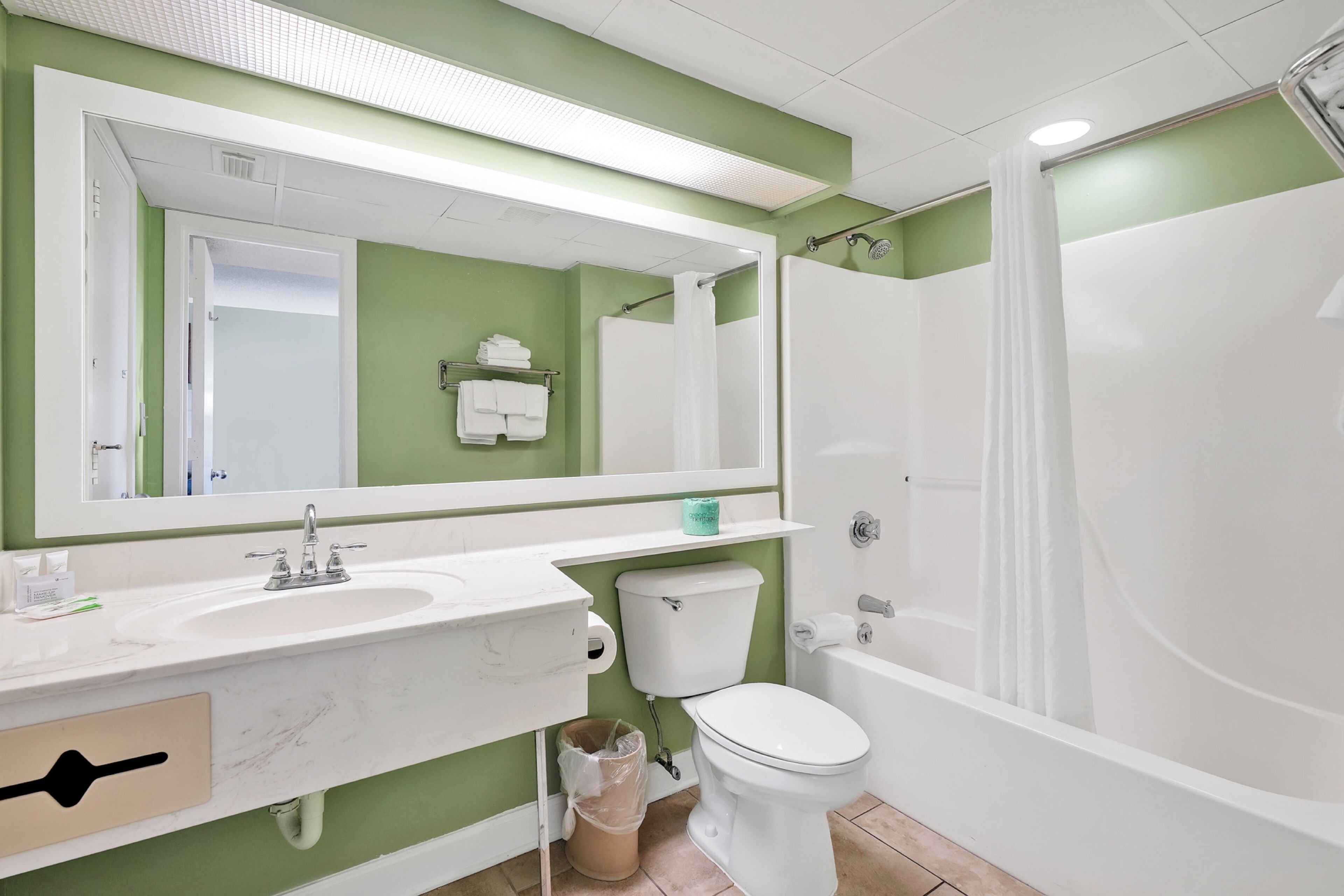 Une salle de bain avec un lavabo, des toilettes et une baignoire, tous de couleur blanche. Un miroir est placé au-dessus du lavabo et un porte-serviettes est fixé au mur.