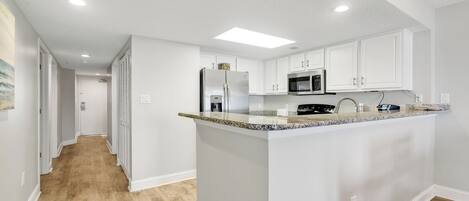 Una cocina moderna con armarios blancos, encimera de granito y electrodomésticos de acero inoxidable.