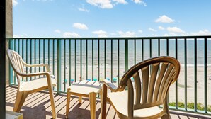 A balcony with two chairs and a table, overlooking a beach with a railing. - Sand Dunes Resort and Suites (Myrtle Beach)