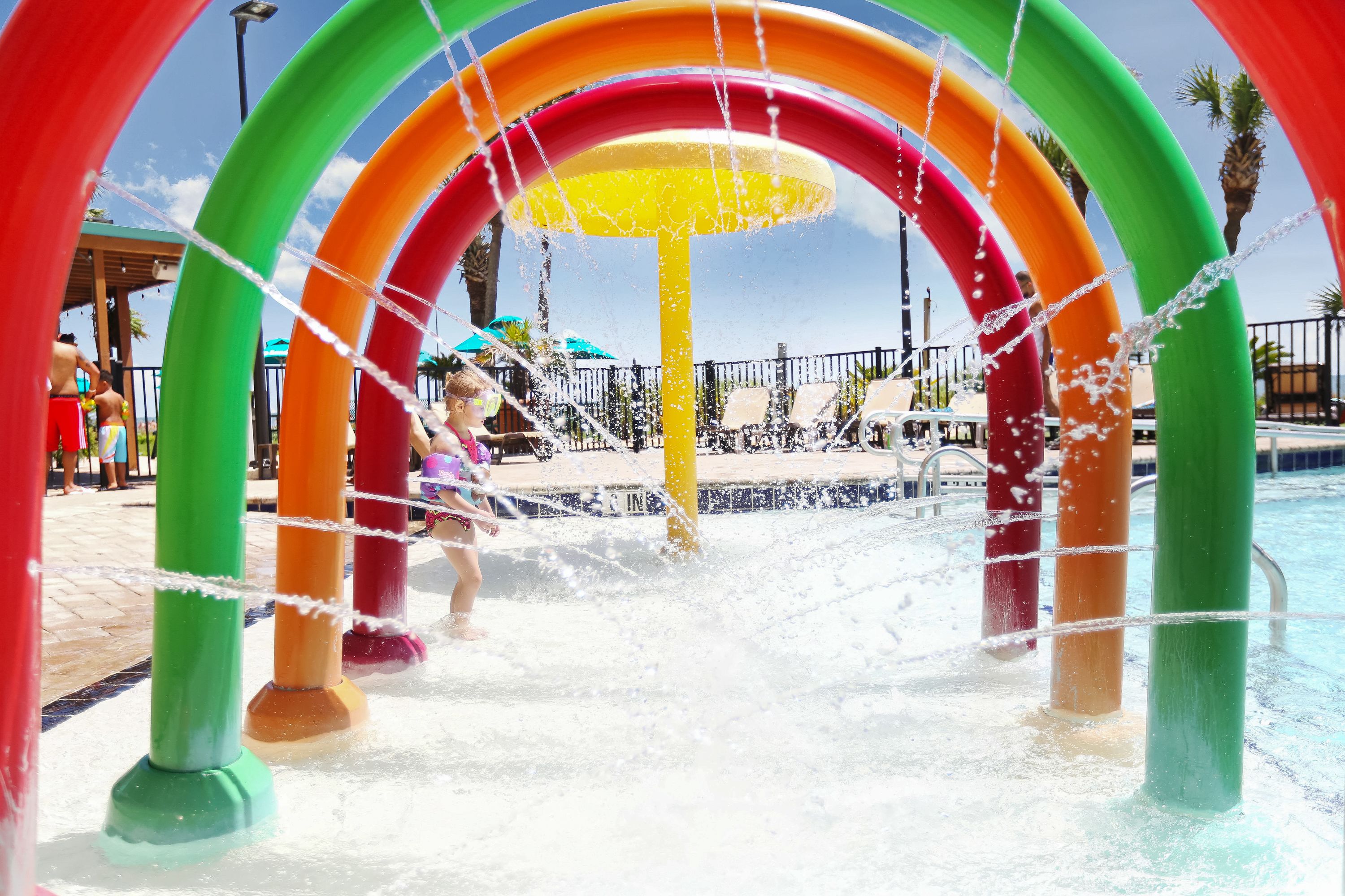 Un espace de jeux aquatiques agrémenté d’arcs colorés et d’une fontaine centrale.