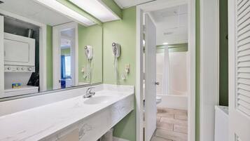 A bathroom with a white sink, a large mirror, two hair dryers mounted on the wall, and a visible shower area.