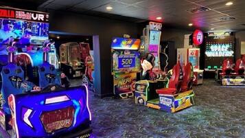 Una sala de juegos recreativos con diversas máquinas, incluyendo un juego de 'Space Invaders' y una máquina con temática 'Nerd'.