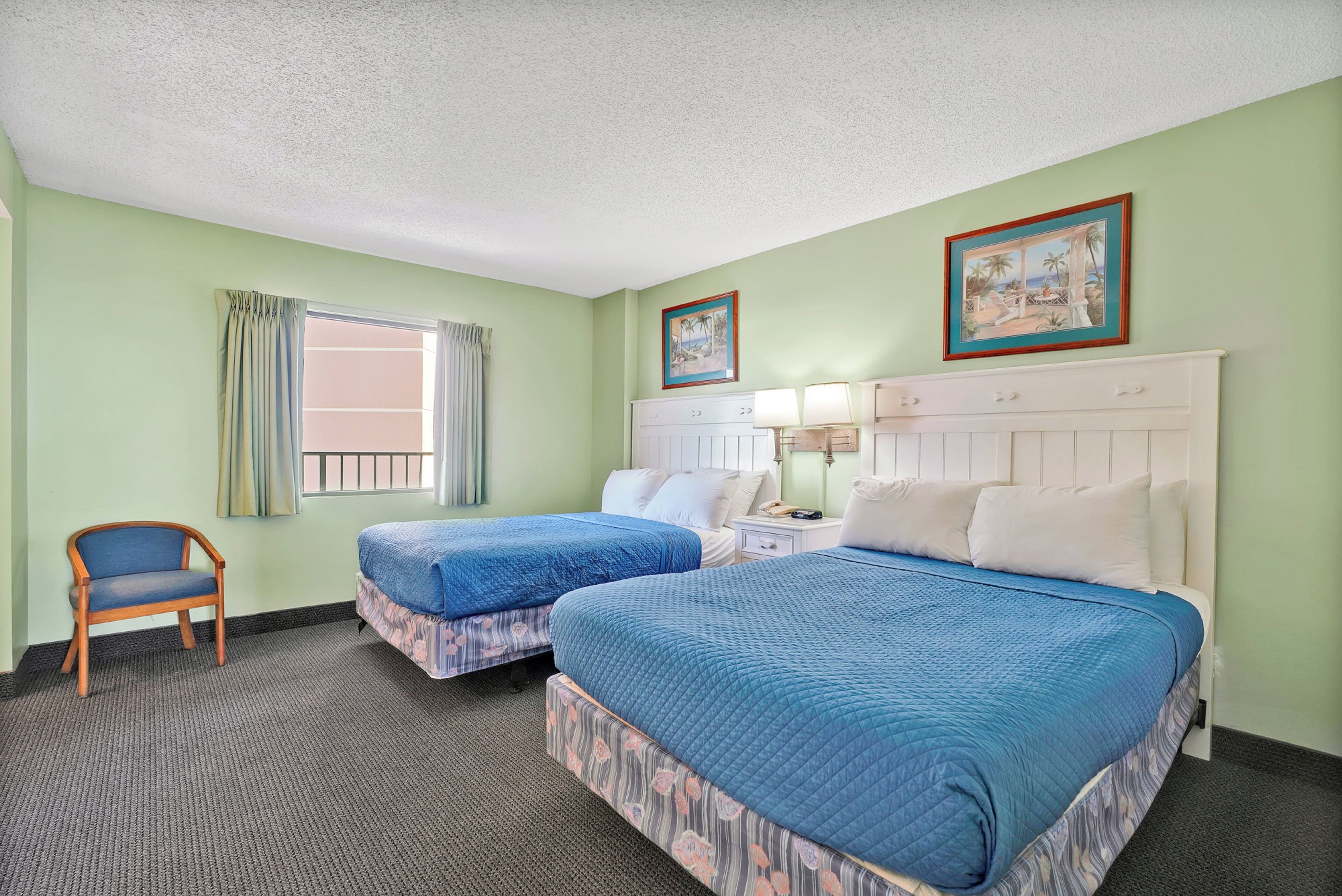 A hotel room with two beds, a chair, a window with curtains, and a painting on the wall.