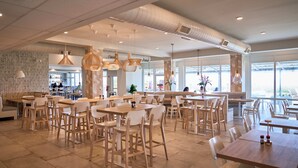 A spacious cafe with multiple tables and chairs, large windows, and hanging pendant lights. - Sand Dunes Resort and Suites (Myrtle Beach)