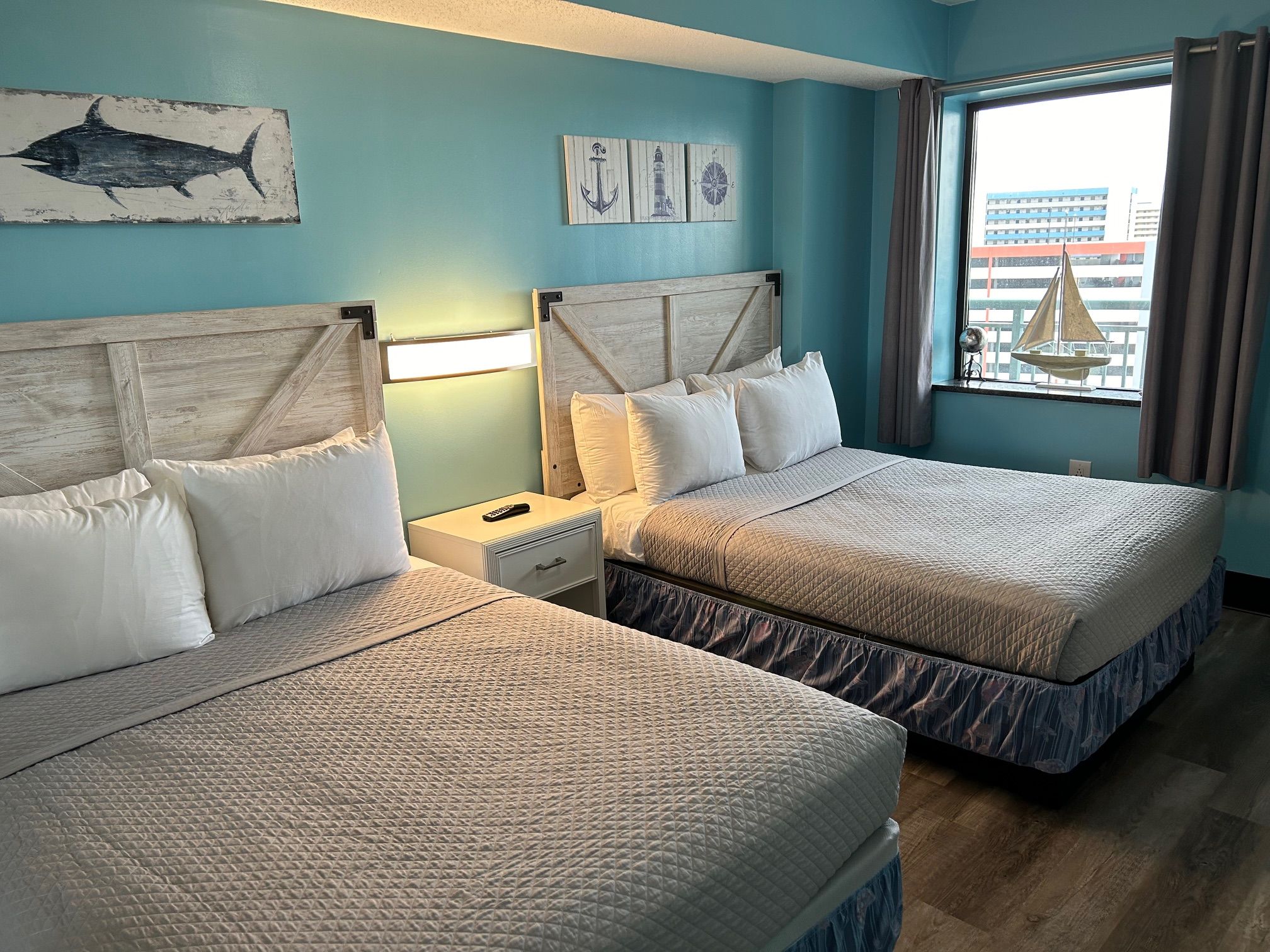 A hotel room with two beds, a nightstand, a lamp, and artwork on the wall.