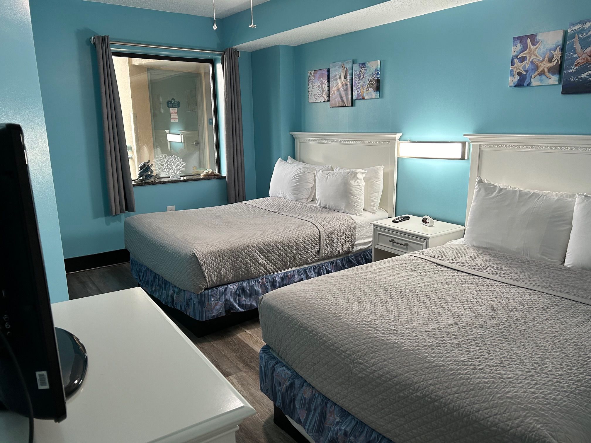 A hotel room with two beds, a desk, and a television.