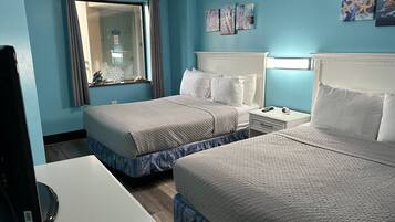 A hotel room with two beds, a desk, and a television.