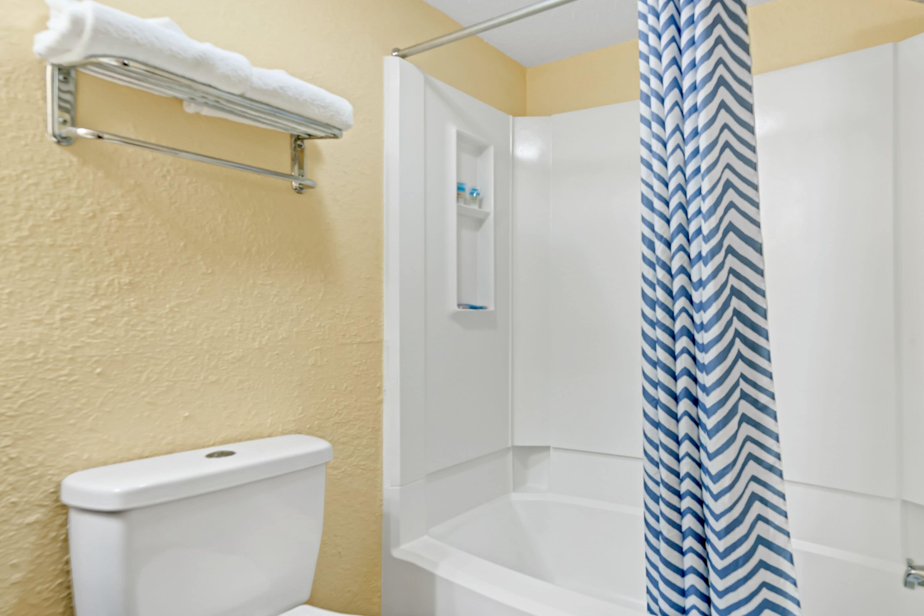 Um banheiro com uma banheira branca, um cortina de chuveiro com padrão azul e branco em zigue-zague e um porta-toalhas com uma toalha branca.