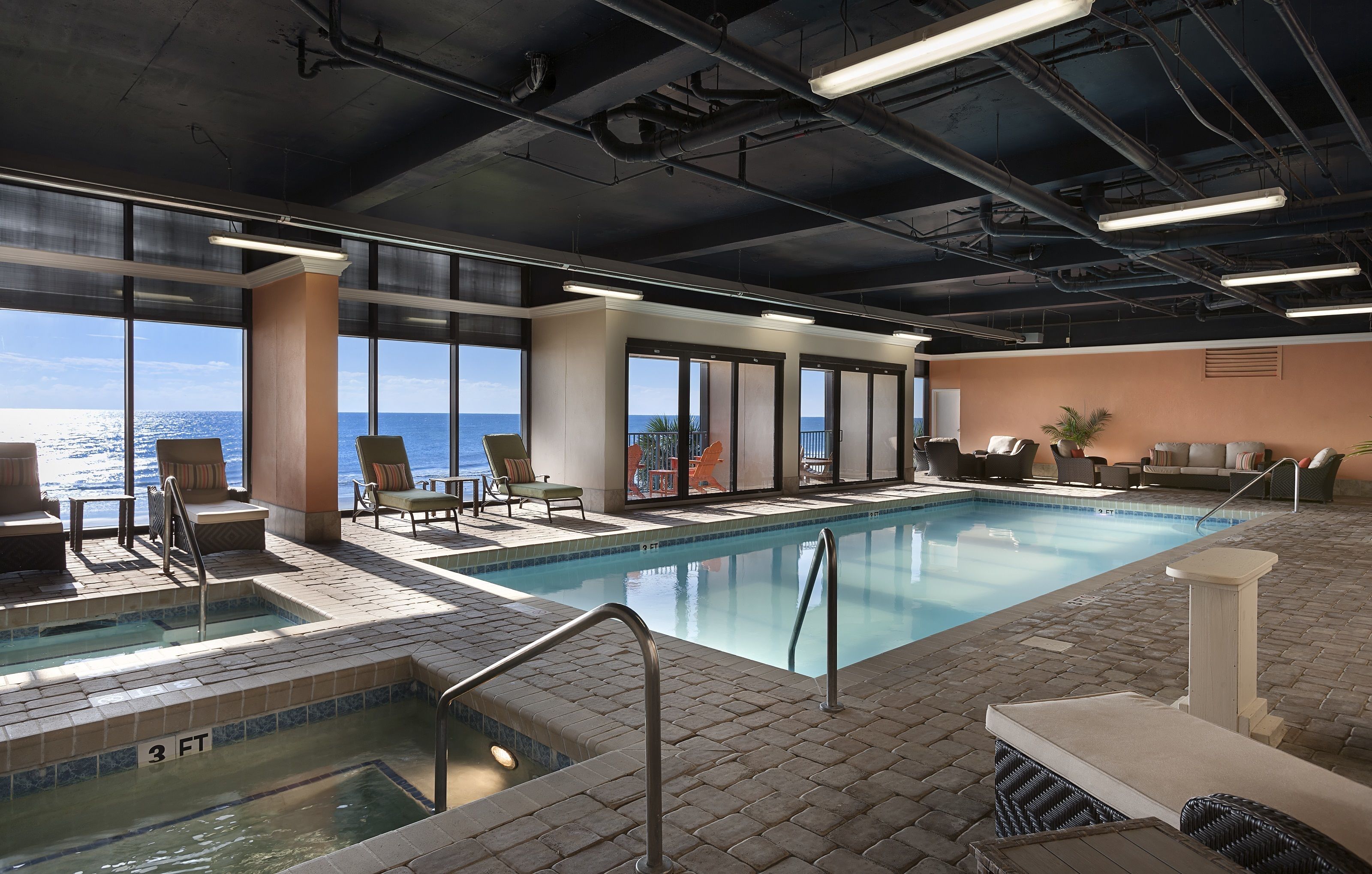 A pool area with a view of the ocean, lounge chairs, and a jacuzzi.