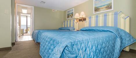 A hotel room with two beds, a hallway leading to a balcony, and a painting on the wall.