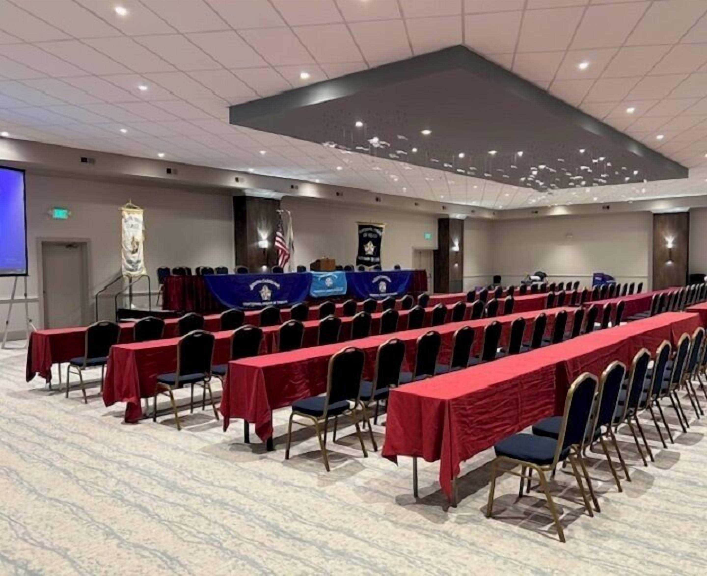 A conference room with rows of tables and chairs, a podium, and a projection screen.