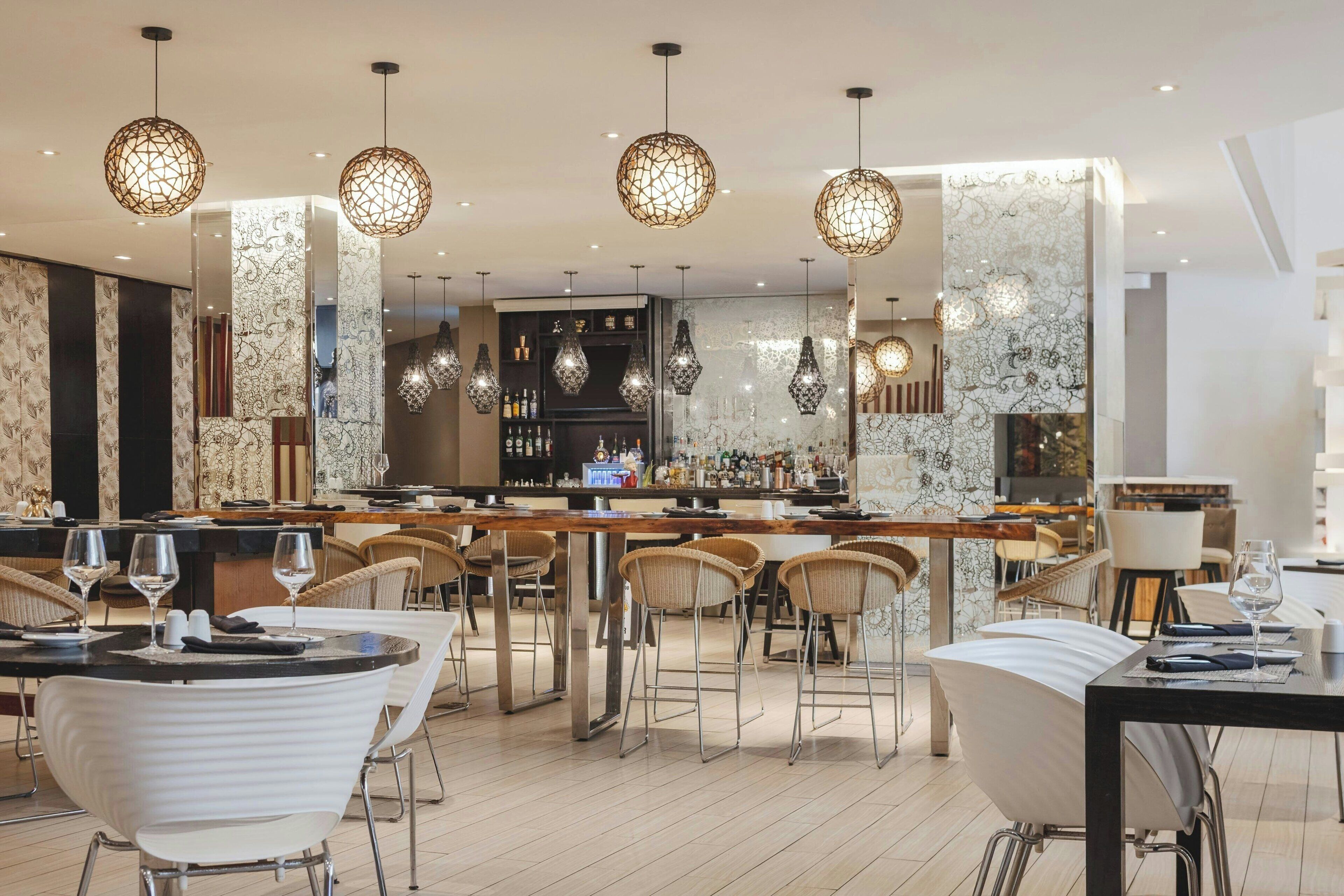 Un espace bar moderne avec des tabourets hauts, un long comptoir et des luminaires décoratifs suspendus.