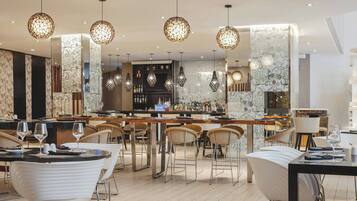 Un espace bar moderne avec des tabourets hauts, un long comptoir et des luminaires décoratifs suspendus.