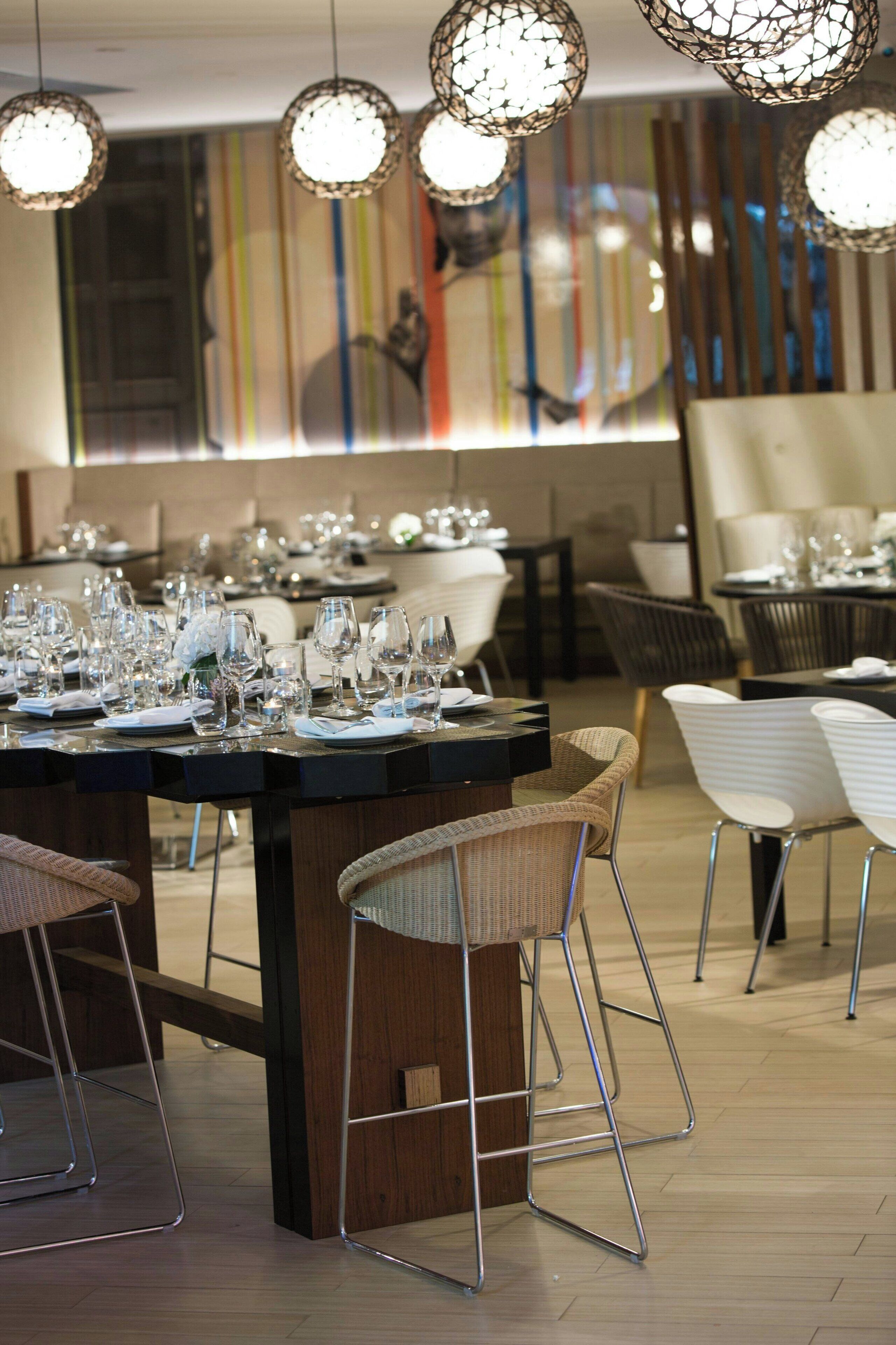 Un restaurante con una larga mesa de comedor, numerosas sillas y lámparas colgantes.