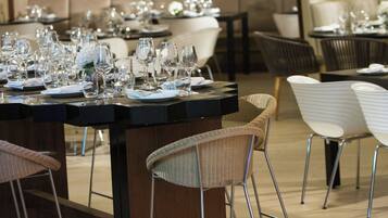 Un restaurante con una larga mesa de comedor, numerosas sillas y lámparas colgantes.