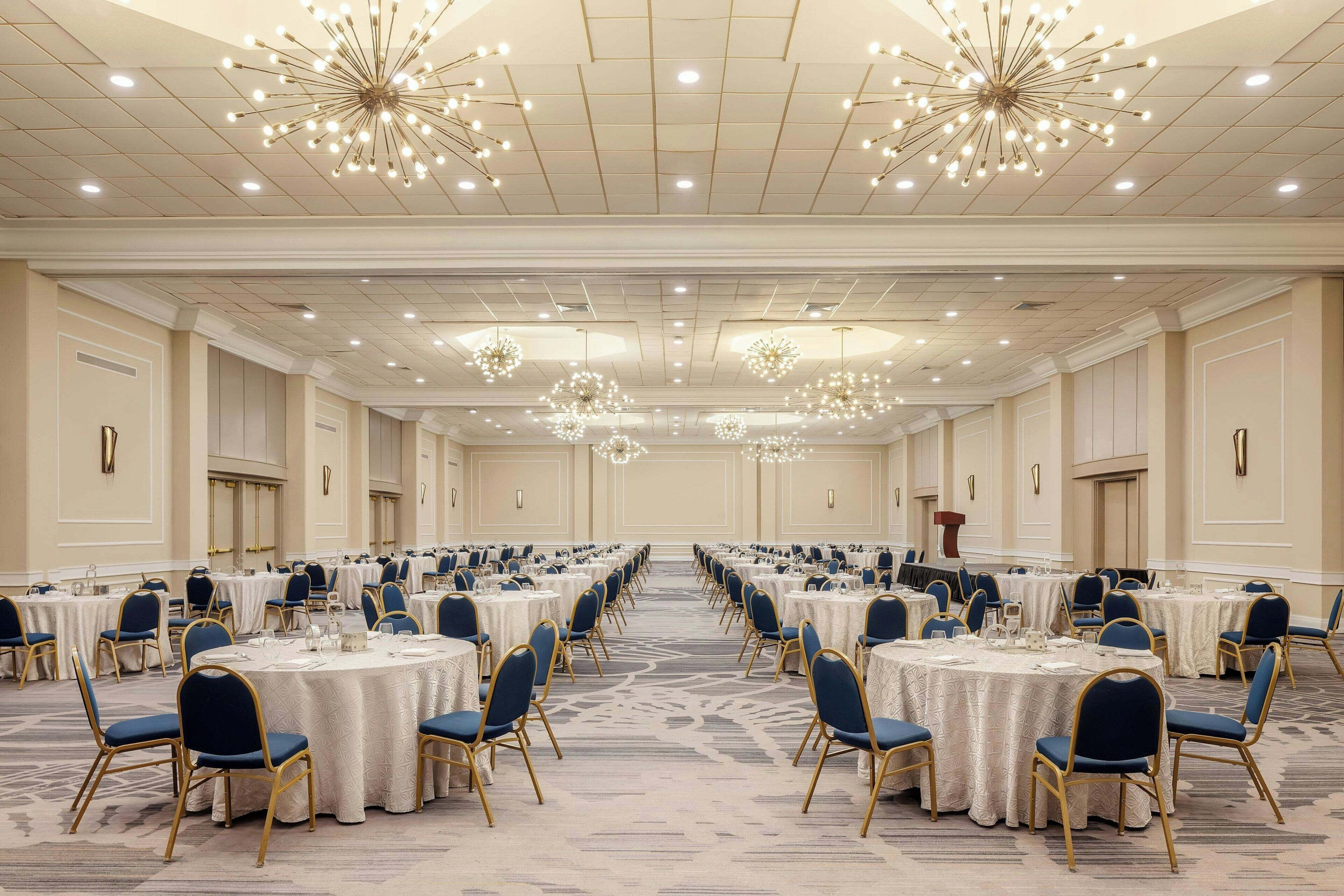 Un amplio salón de banquetes con mesas redondas, sillas azules y candelabros.