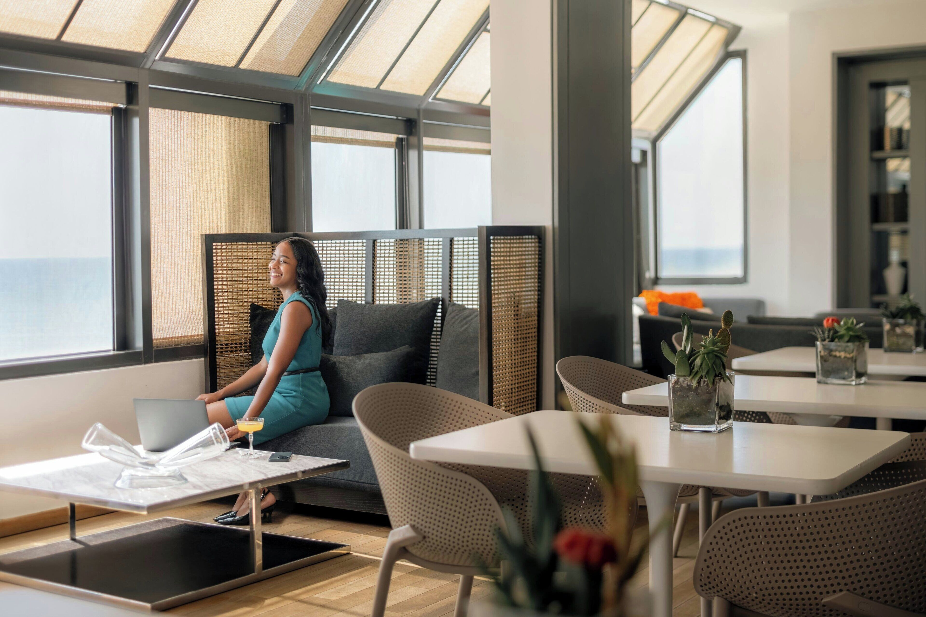 Ein modernes Interieur mit einer Sitzecke, einem Tisch mit einem Laptop und Meerblick durch große Fenster.