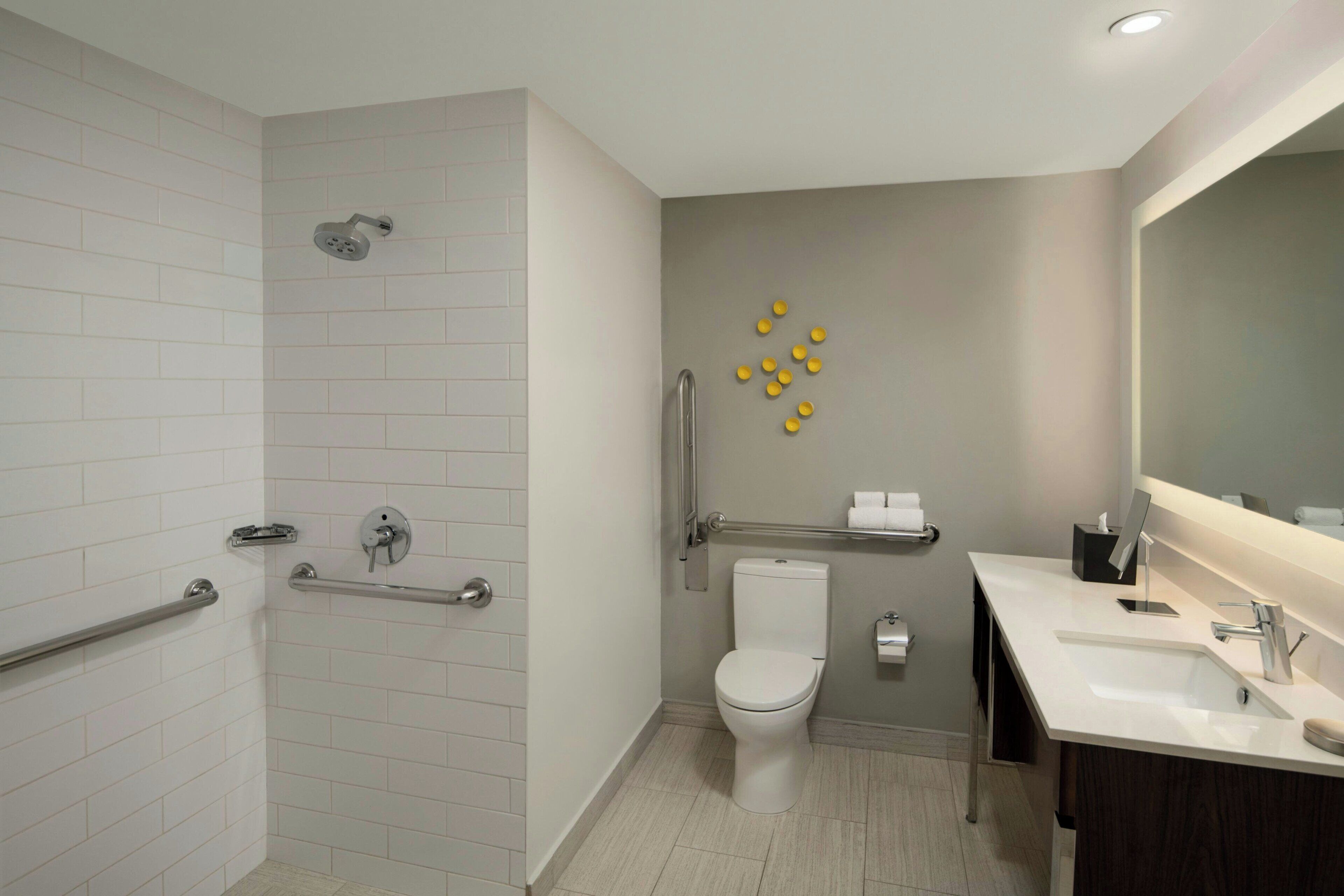 A modern bathroom with white tiles, a shower, a toilet, and a sink with a mirror.