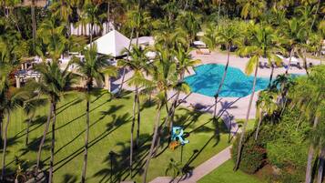 An aerial view of a resort with a swimming pool, palm trees, and a white building.
