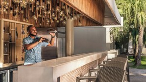 A bar area with a wooden ceiling and hanging light fixtures, a counter with a modern design, and outdoor seating with wicker chairs. - Renaissance Santo Domingo Jaragua Hotel & Casino (Santo Domingo)