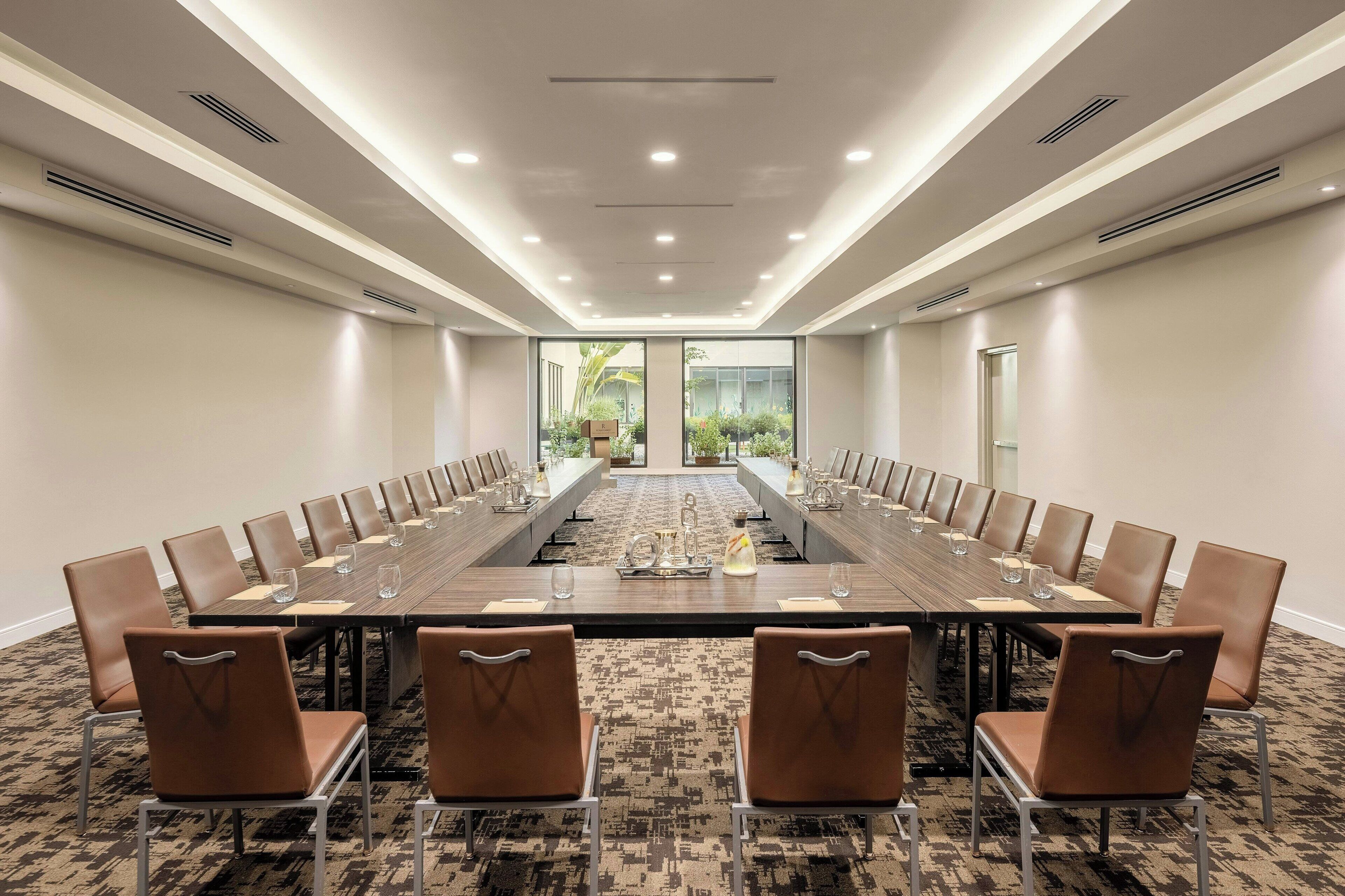 A conference room with a long table, brown chairs, and a carpeted floor.