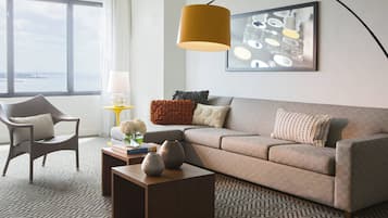 A modern living room with a sofa, armchair, and coffee table, a large window with a view, and a hanging lamp.