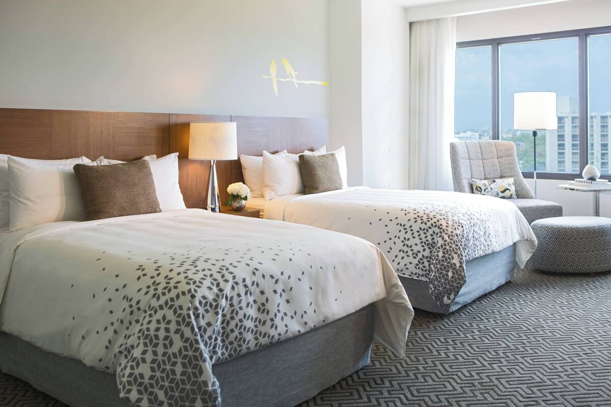 Une chambre d’hôtel avec deux lits, une grande fenêtre donnant sur un paysage urbain et une vue sur la ville.