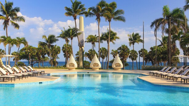 A swimming pool with lounge chairs and palm trees, surrounded by a clear sky. - Renaissance Santo Domingo Jaragua Hotel & Casino (Santo Domingo)